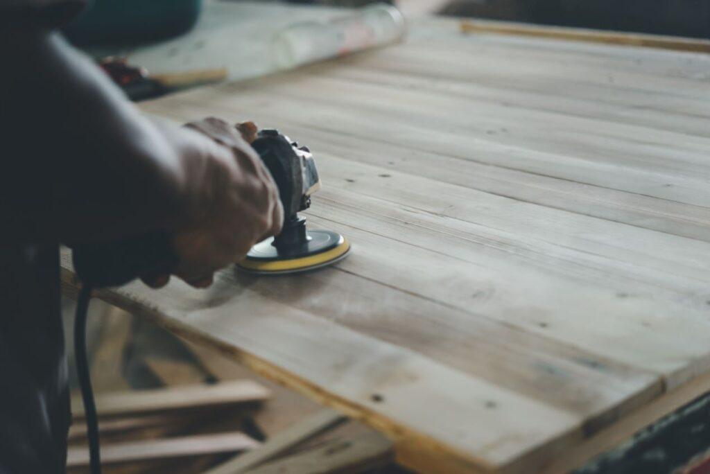 Handwerkliches Schleifen einer Holzoberfläche – Detailarbeit für ein nachhaltiges und ästhetisches Holzlager im Garten.